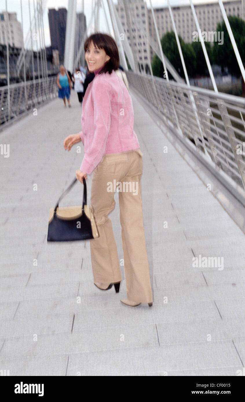 Femmina lunghezza di spallamento brunette capelli, indossando un top Malva, Rosa  giacca e pantaloni beige, camminando per il millennio Foto stock - Alamy