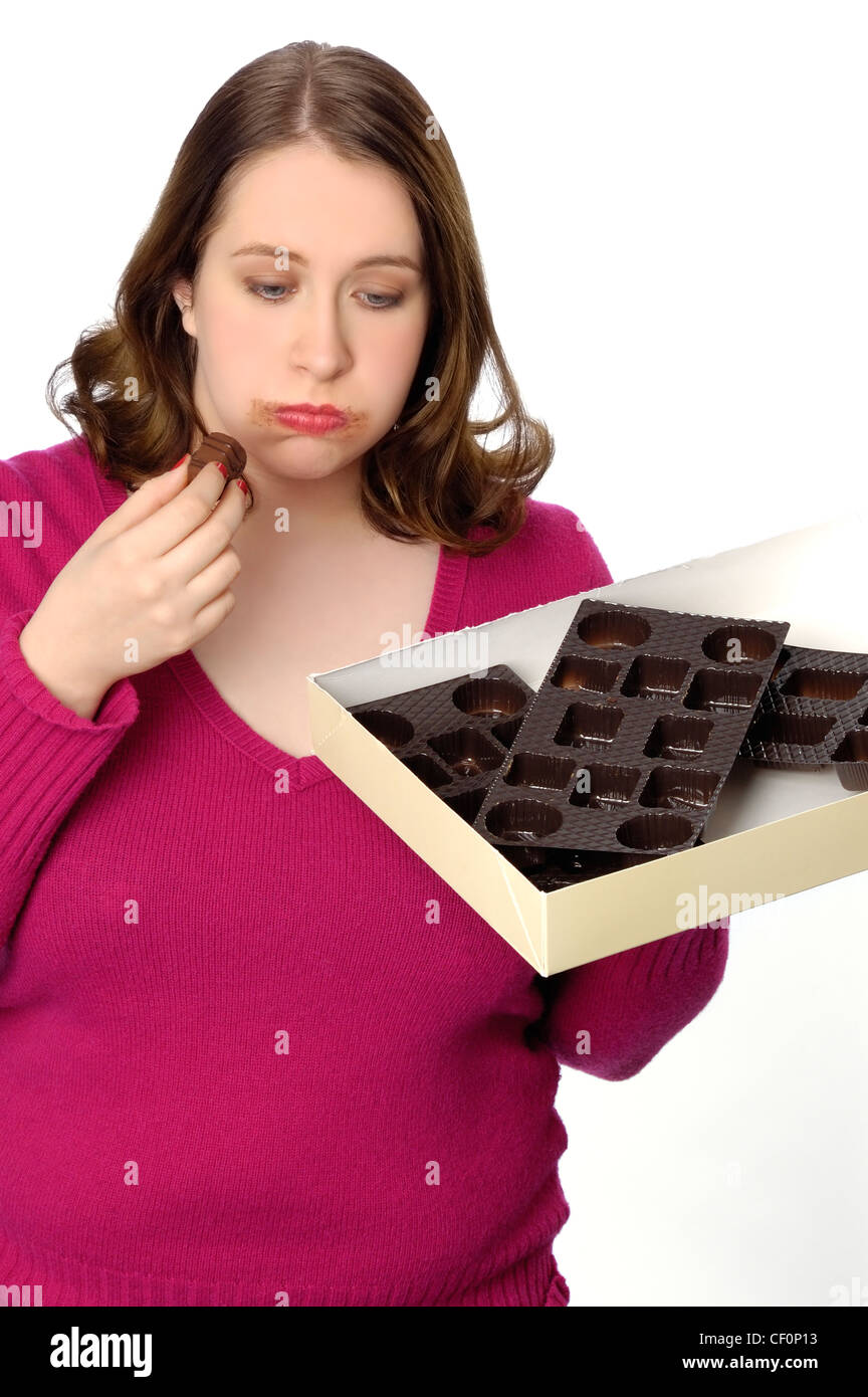 Foto divertente di una donna che ha mangiato una grande scatola di cioccolatini e è la sensazione di malessere e la pancia gonfia. Foto Stock