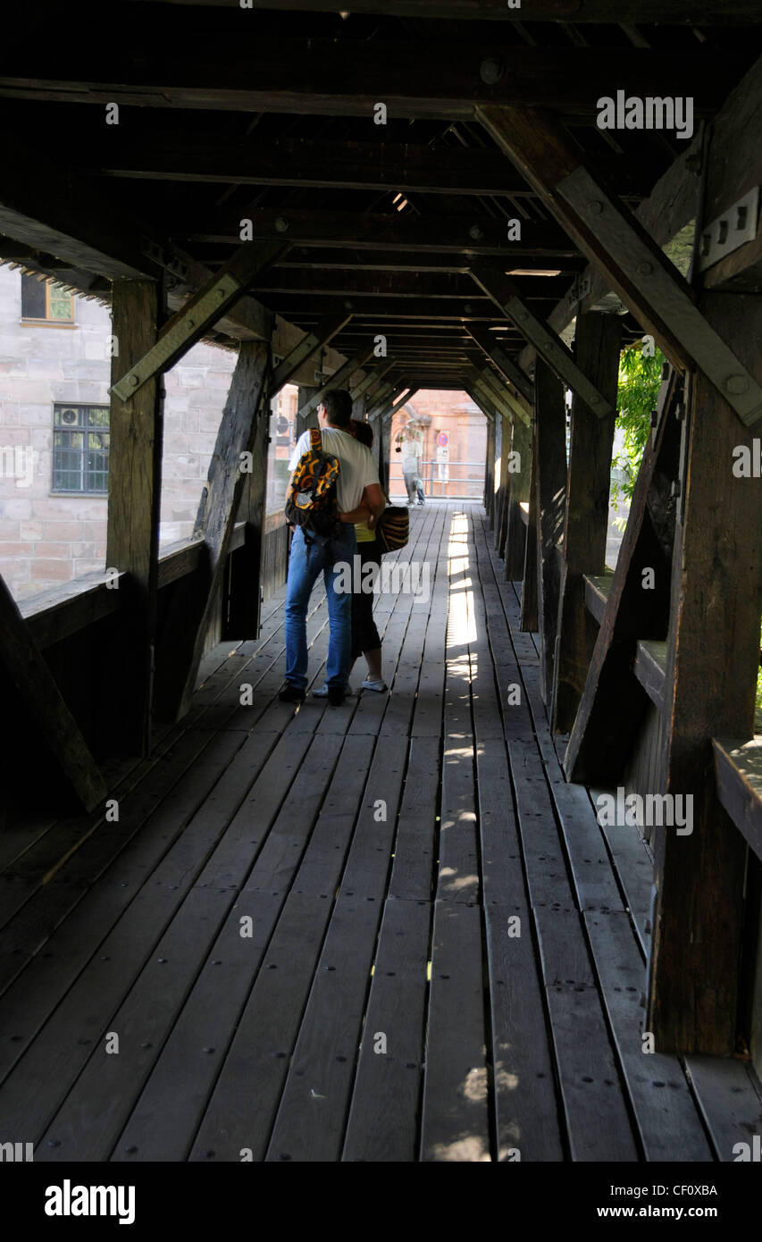 Un paio di turisti sul ponte pedonale in legno chiamato 'Executioner's Walk' attraverso il fiume Pegnitz a Norimberga, Germania. Il lungo rosso-piastrellato Foto Stock