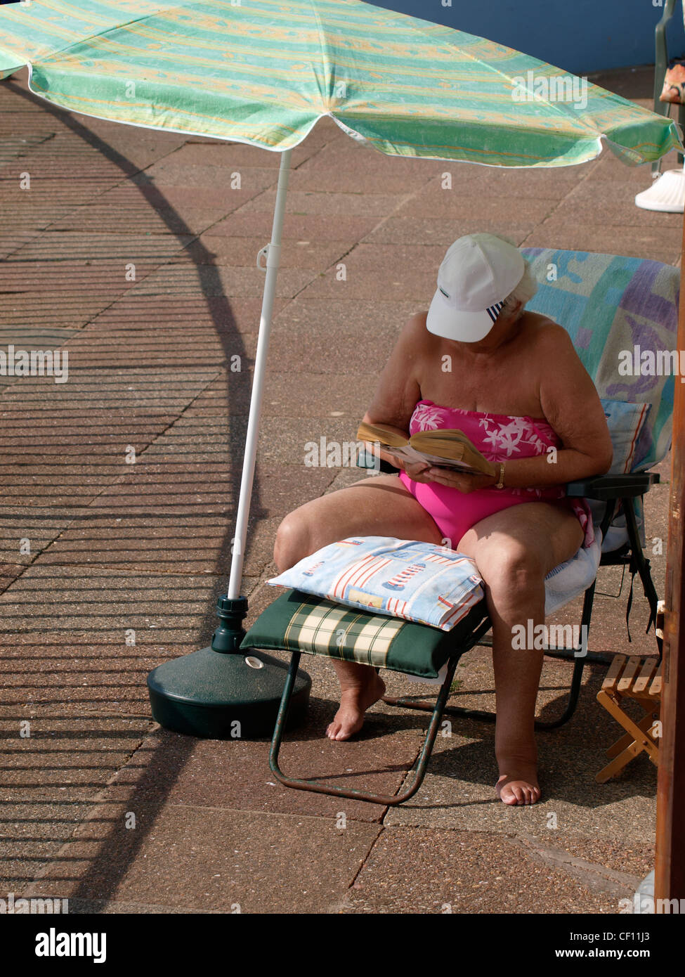 Vecchia donna sotto un ombrellone la lettura di un libro, Cornwall, Regno Unito Foto Stock