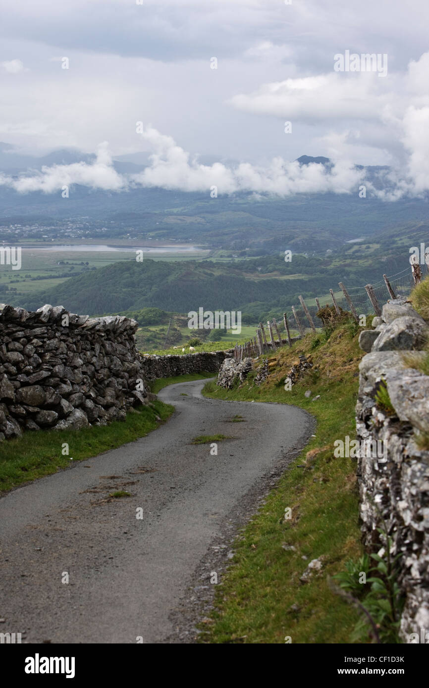 Via unica strada in discesa di avvolgimento tra tradizionali pareti in pietra nel Parco Nazionale di Snowdonia. Foto Stock