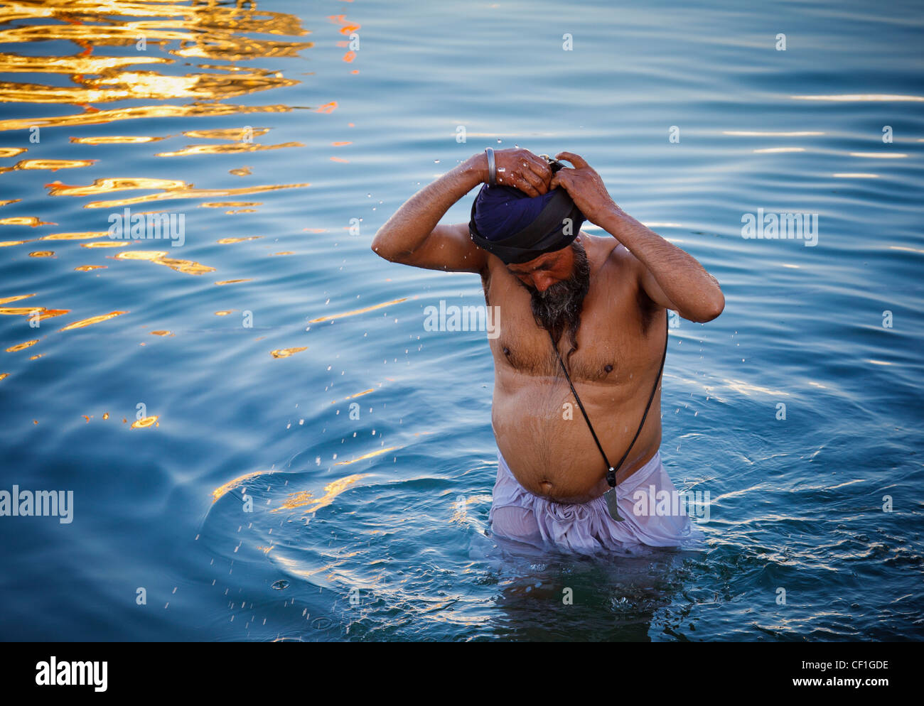 Un uomo Sikh prende un bagno in Amrit Sarovar, la piscina che circonda il tempio d'oro di Amritsar Punjab, India Foto Stock