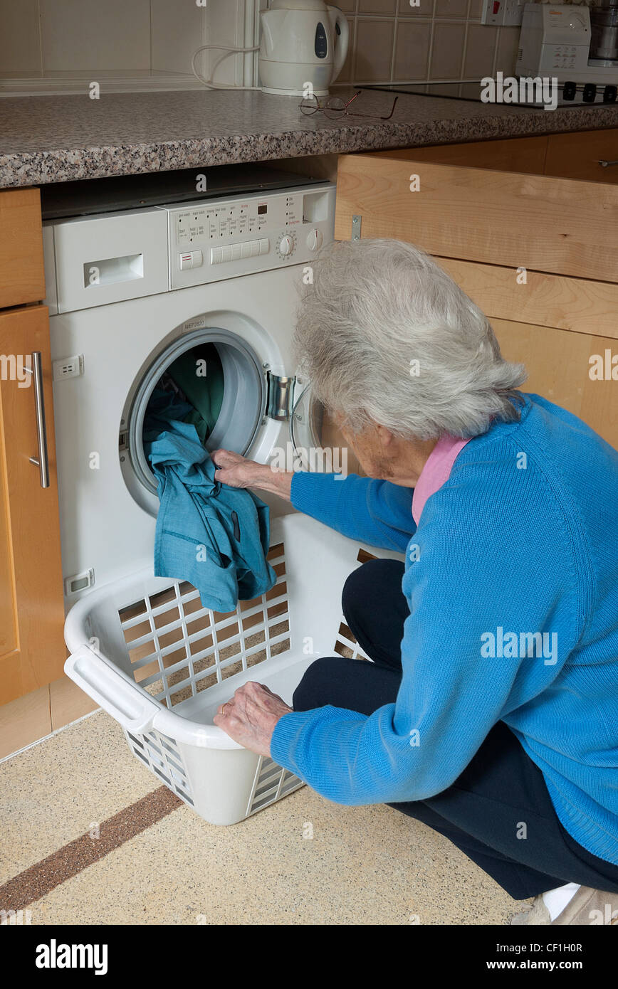 Signora il caricamento di una macchina di lavaggio in una camera di servizio o di utilità, Inghilterra, Regno Unito. Foto Stock