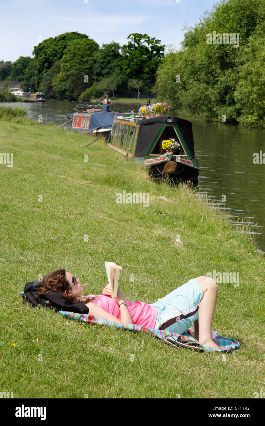 Una giovane donna di relax con un libro sulla sponda del fiume del fiume Tamigi a Abingdon Bridge. Foto Stock