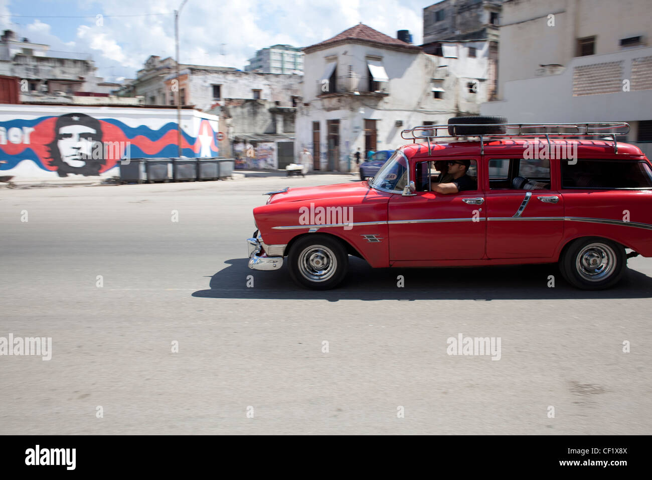 Red classic car essendo guidato su strada a l'Avana, Cuba con l'immagine di Che Guevara in background Foto Stock