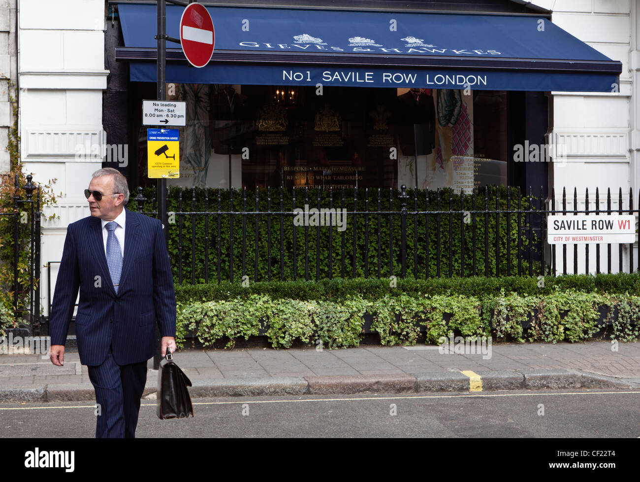 Un imprenditore che indossa un perno tuta a strisce attraversamento Savile Row fuori Gieves & Hawkes, bespoke sarti. Foto Stock