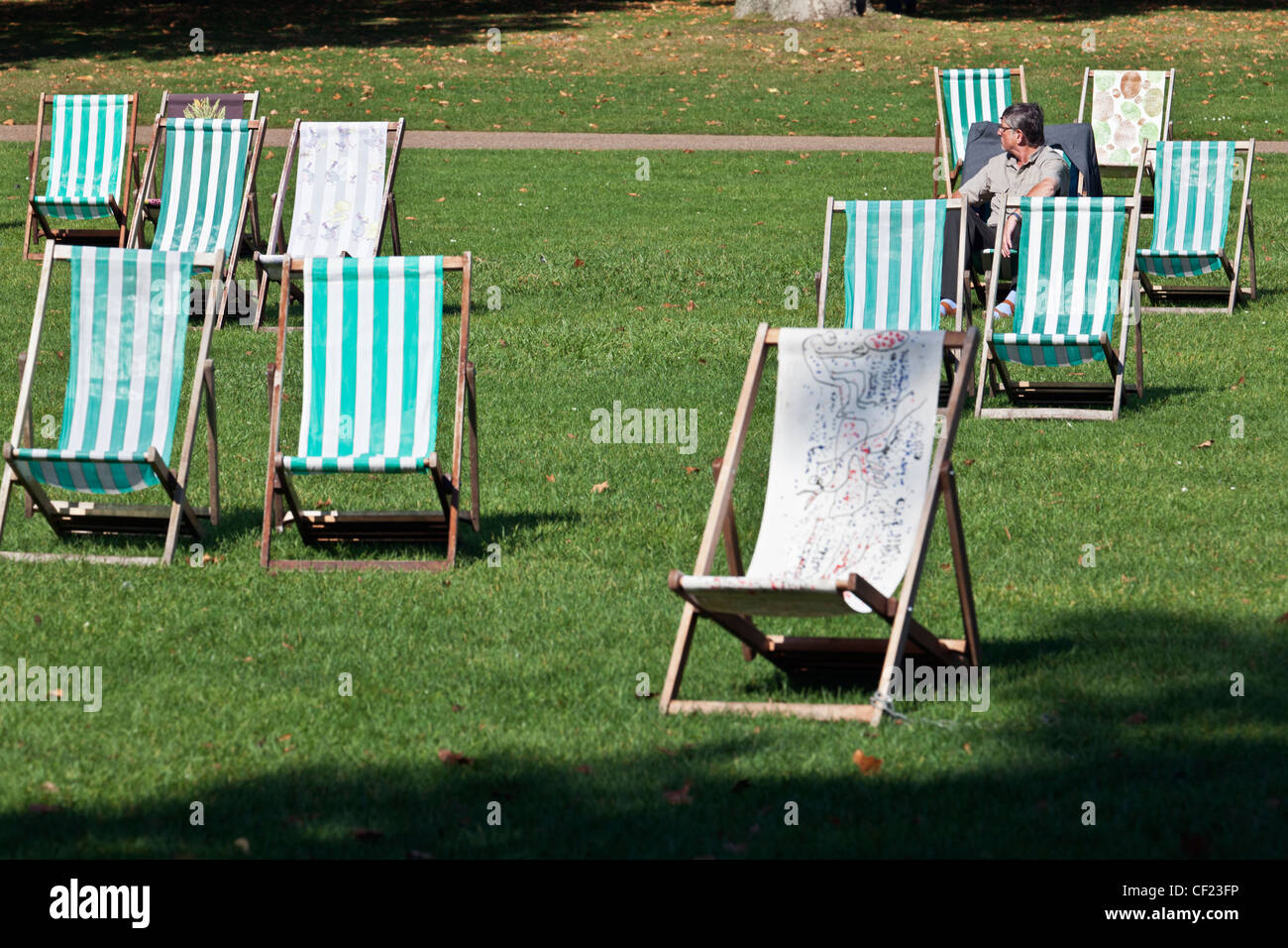 Un uomo seduto in una sedia a sdraio in St James Park. Foto Stock
