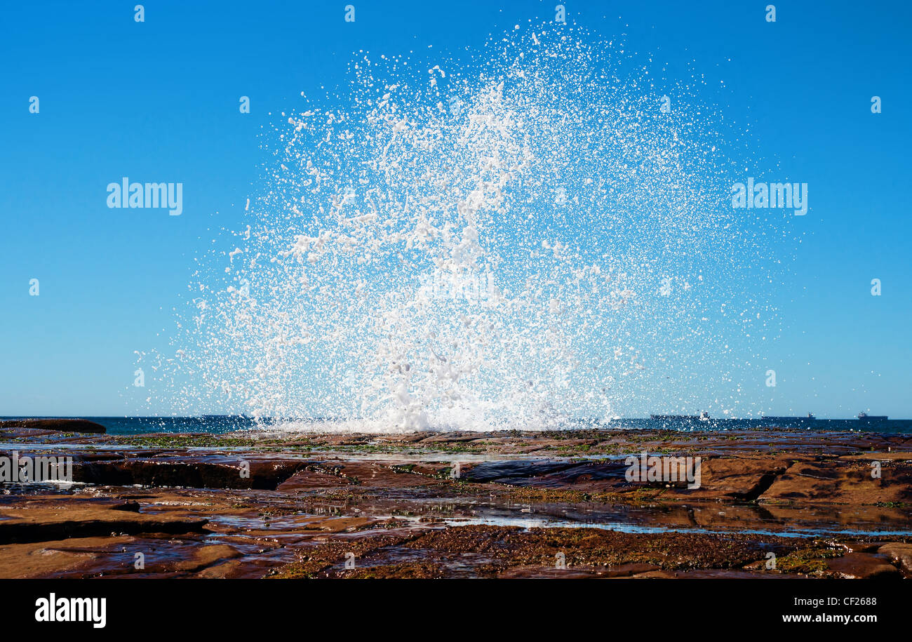 Grande splash come un onda colpisce le rocce lungo la costa Foto Stock