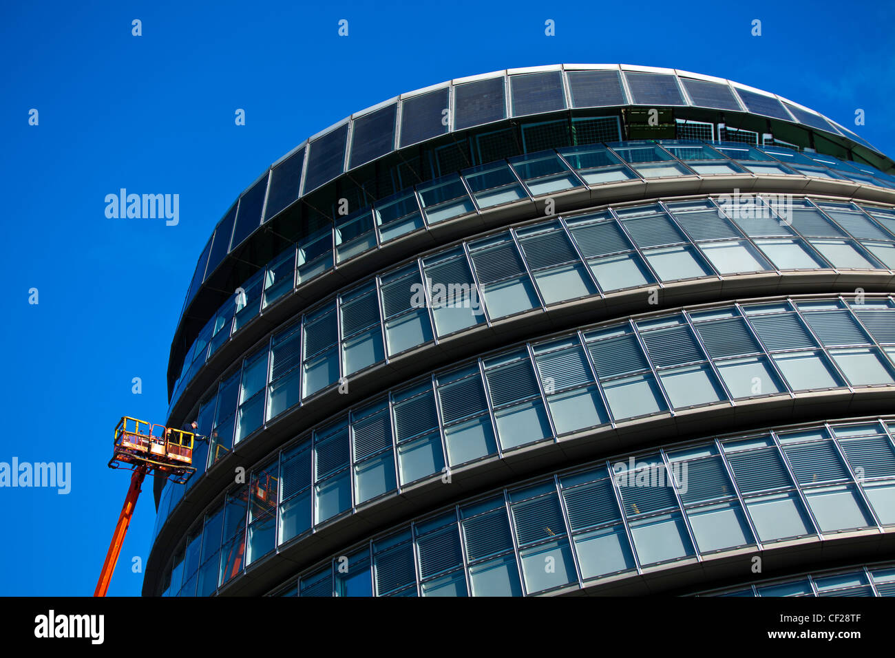 Un operaio eseguire la manutenzione da un cherry picker su una finestra del Municipio, casa della Greater London Authority (GLA) compr Foto Stock