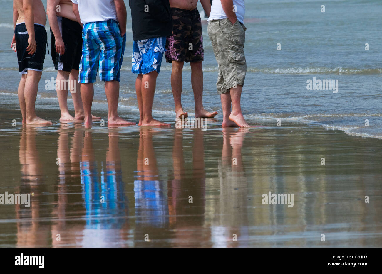 Un gruppo di turisti maschio in piedi sul foreshore di una spiaggia con la bassa marea. Foto Stock