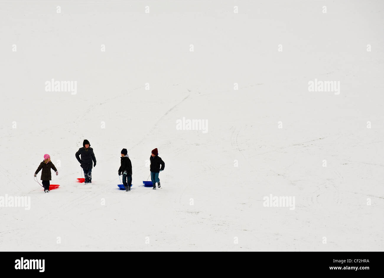I bambini a piedi con i loro slittini fino una coperta di neve pendenza. Foto Stock