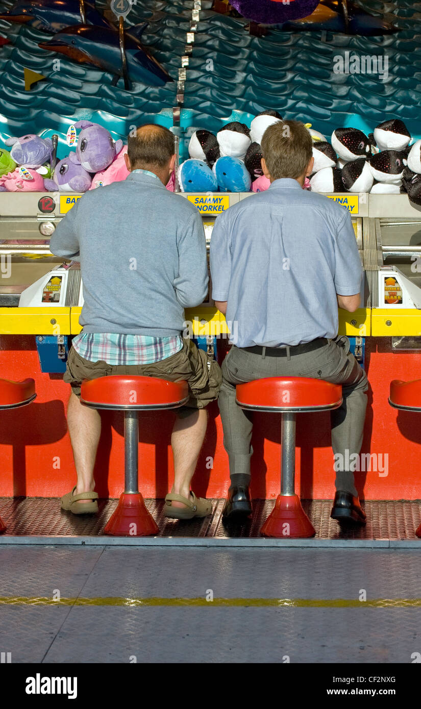 Due uomini seduti su sgabelli giocando a un gioco a una fiera sul molo di Brighton. Foto Stock