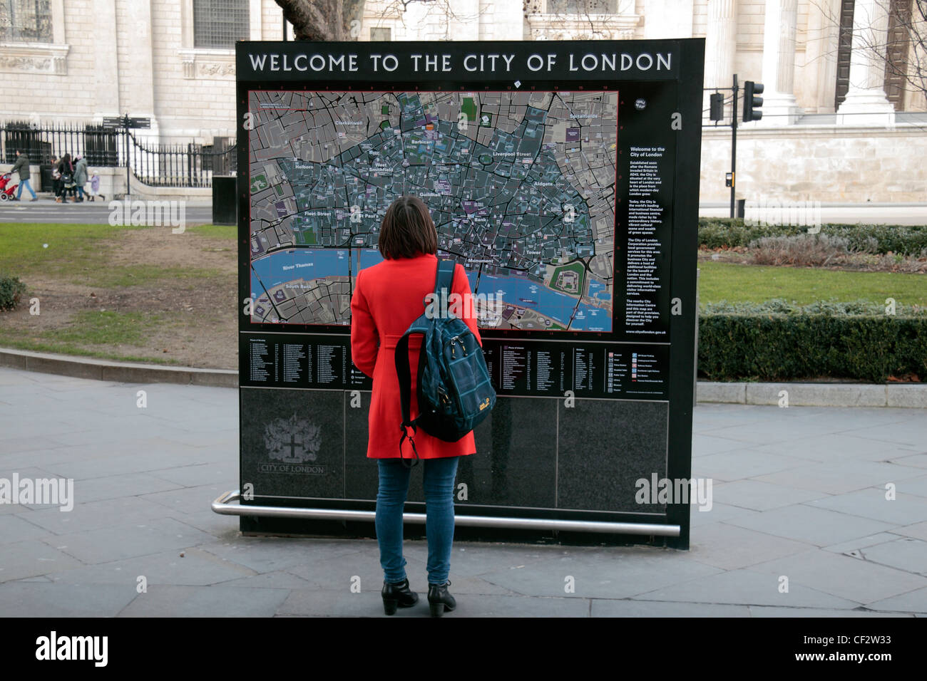 Un turista femminile in un colore rosso brillante rivestire in piedi di fronte a una grande città di Londra mappa turistica vicino alla Cattedrale di St Paul London, Regno Unito Foto Stock