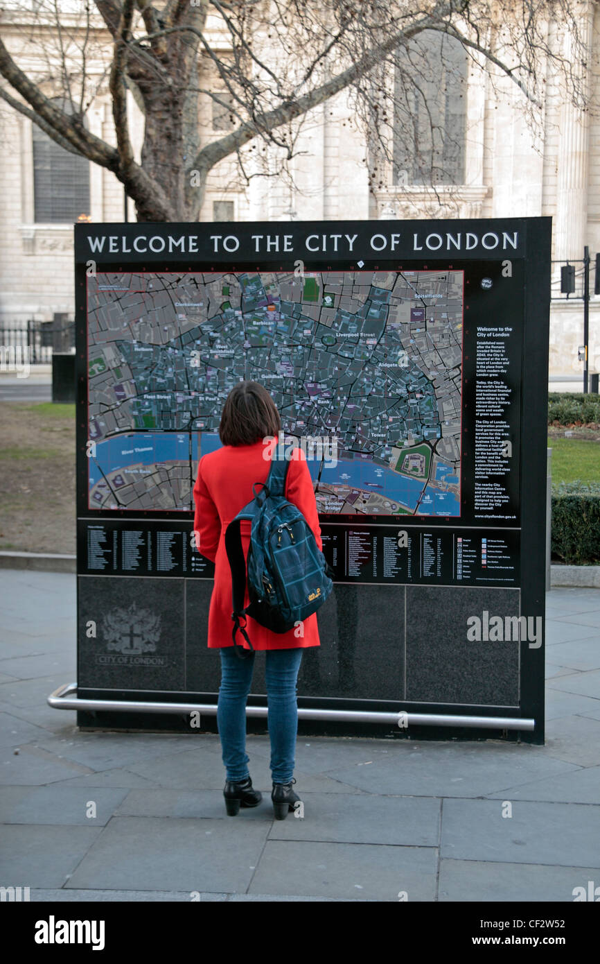 Un turista femminile in un colore rosso brillante rivestire in piedi di fronte a una grande città di Londra mappa turistica vicino alla Cattedrale di St Paul London, Regno Unito Foto Stock