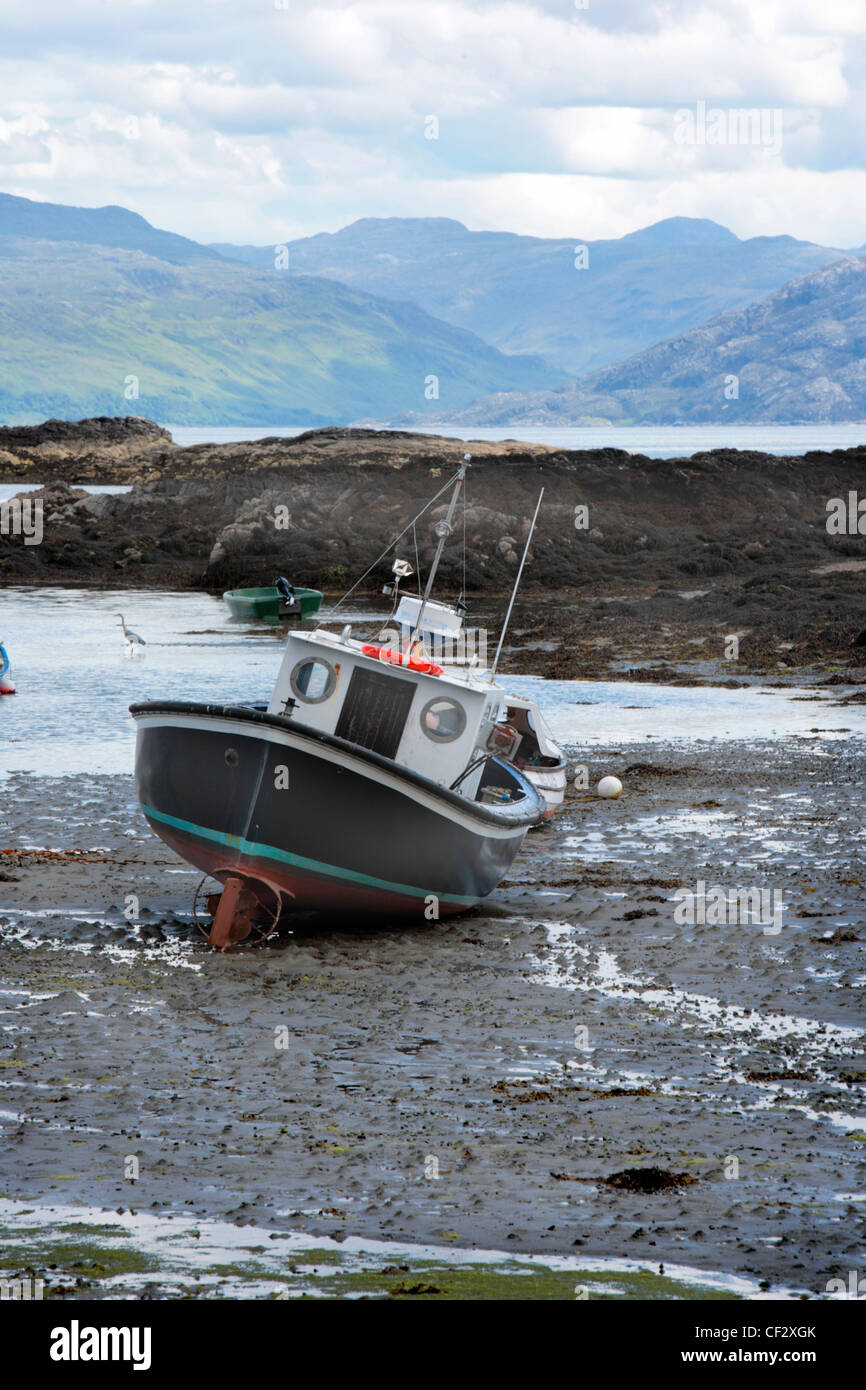 Una piccola barca da pesca sulle velme e un airone guadare in background a Ardvasar sull'Isola di Skye. Foto Stock