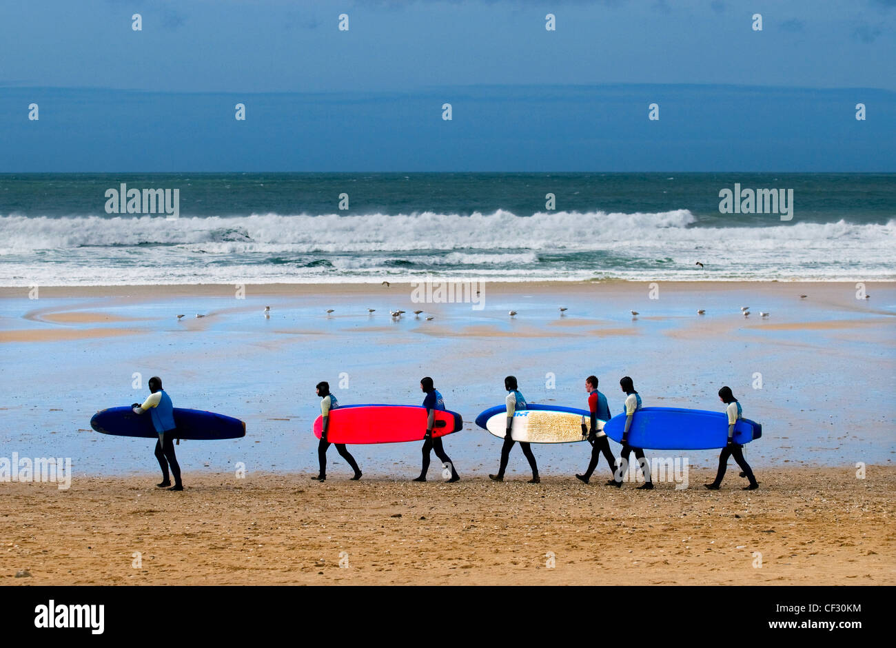 Surfers camminando in una linea che trasporta le loro tavole da surf attraverso Fistral Beach. Foto Stock