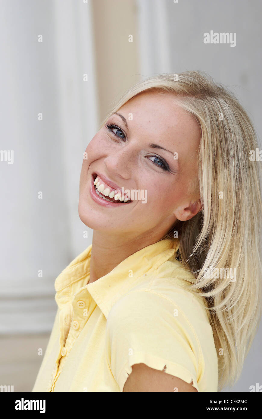 Femmina lunghi capelli biondi, indossando un pallido giallo in alto il collare e manicotti sfilacciata naturale e make up, sorridente verso la telecamera Foto Stock