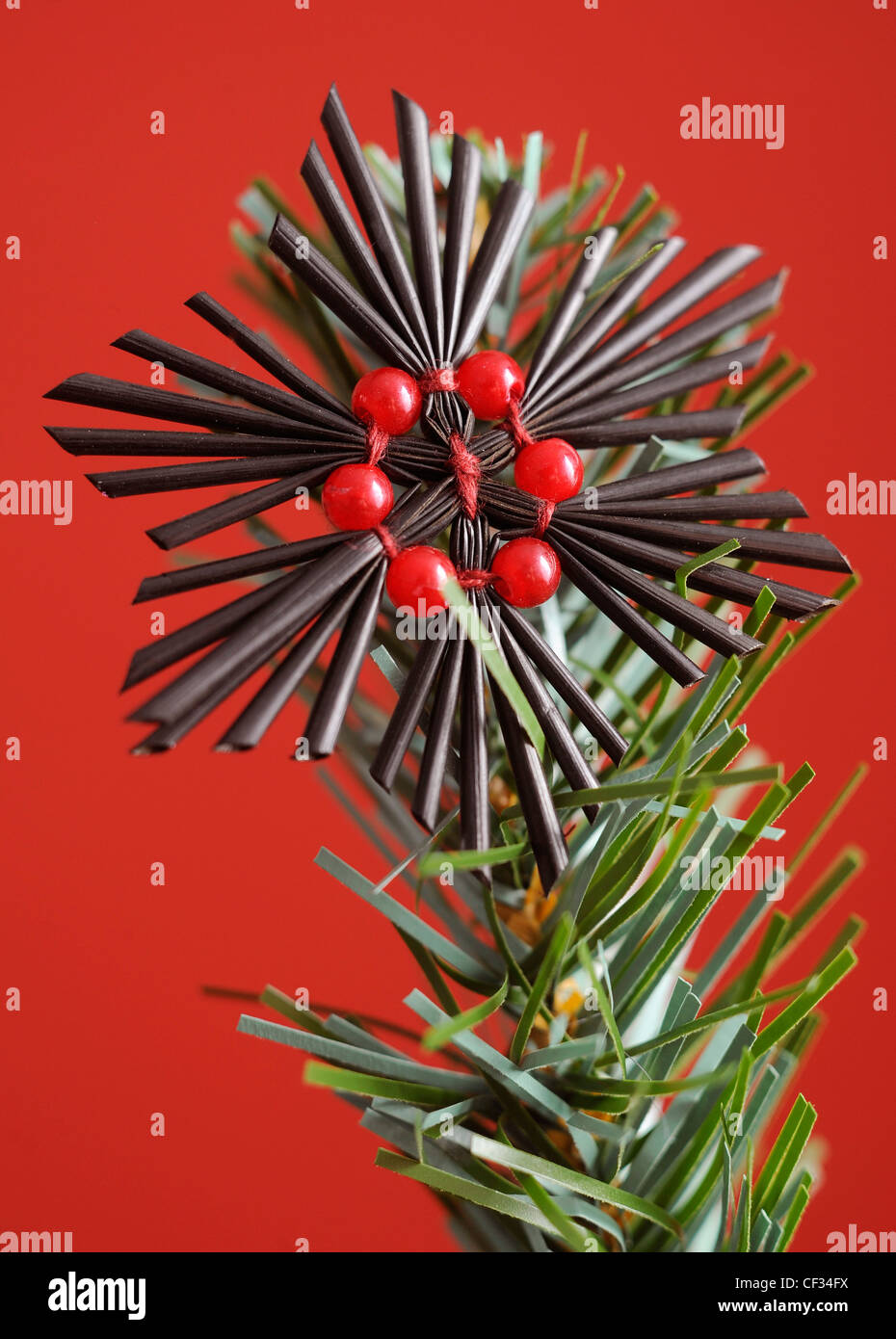 Un nero e rosso di natale a forma di spirale tessuto addobbi per l'albero all'estremità di un albero di natale ramo, con uno sfondo rosso Foto Stock