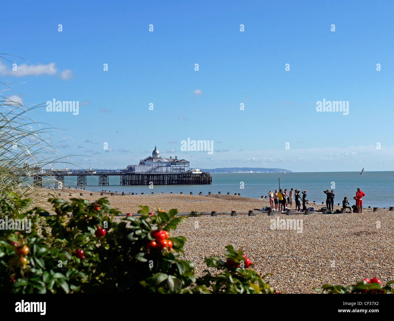 Una classe preparando per una lezione di sport acquatici sulla spiaggia di ciottoli a Eastbourne con il molo in background. Foto Stock