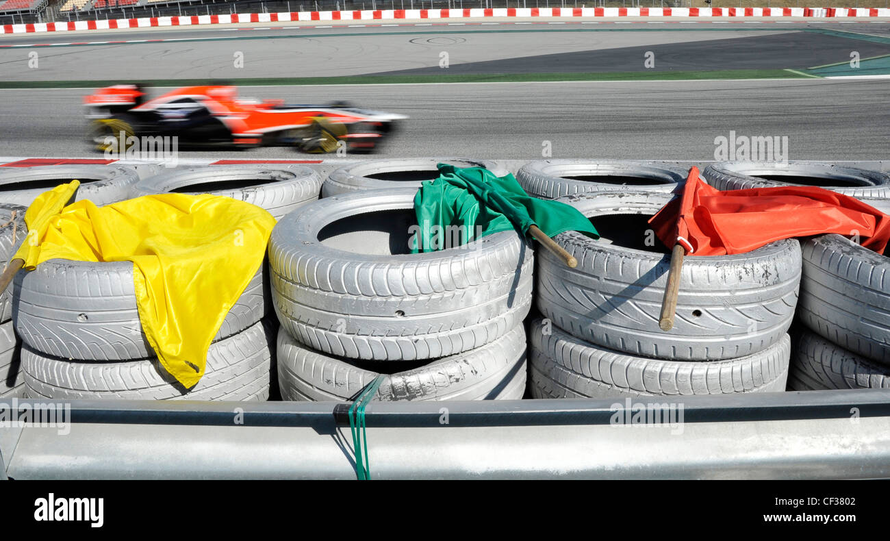 La vettura arancione di Formula 1 accelera con bandiere di segnalazione gialle, verdi e rosse sull'autodromo Foto Stock