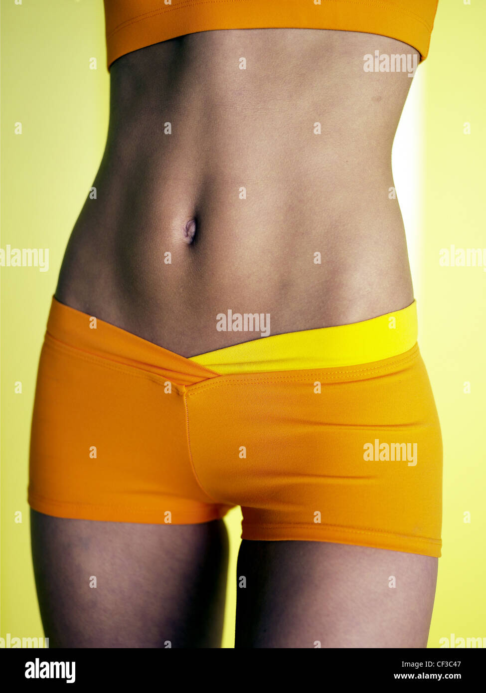 Indossare femmina arancione tagliata in alto e stretto pantaloncini di colore arancione, mostrando pancia piatta Foto Stock