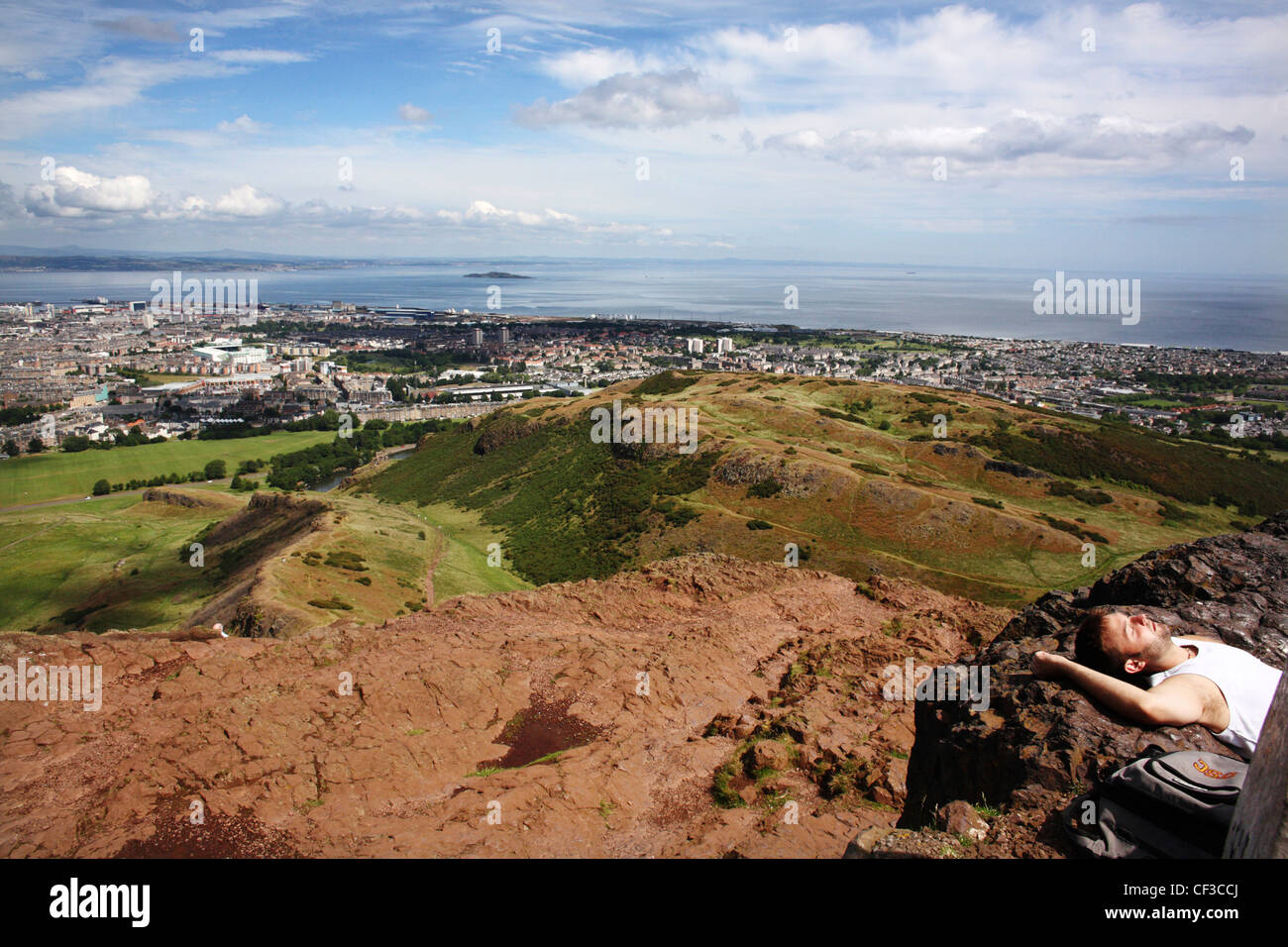 Un uomo a prendere il sole sulla Arthur' Seat si affaccia Edimburgo e il Firth of Forth. Foto Stock