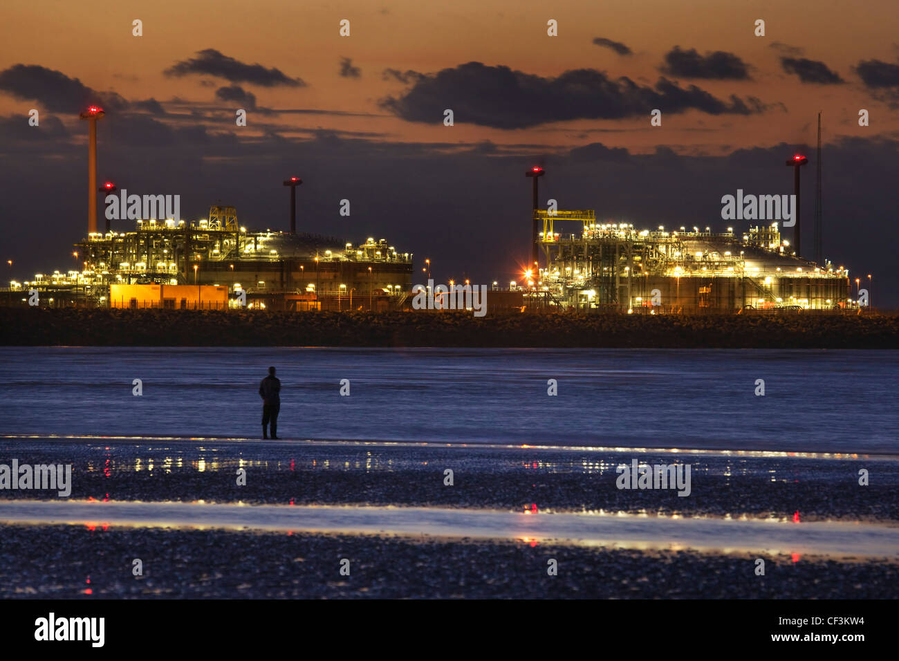 Uomo che guarda dalla spiaggia illuminata a gas terminale a Zeebrugge Nord porta a mare al tramonto, Belgio Foto Stock