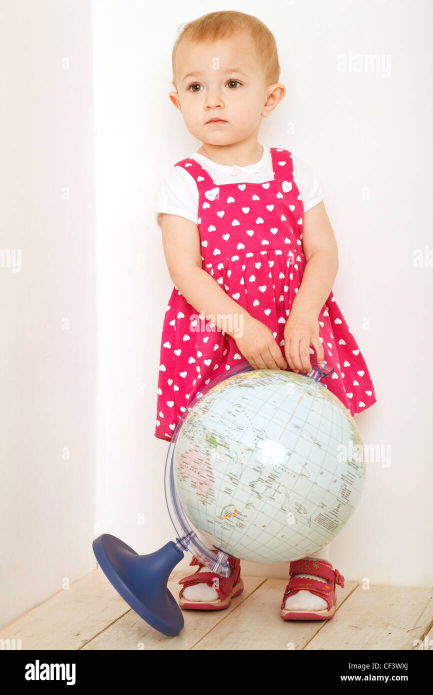 Bambina in abito rosso stadning a piena altezza azienda globo in mani indoor. Formato verticale. Foto Stock