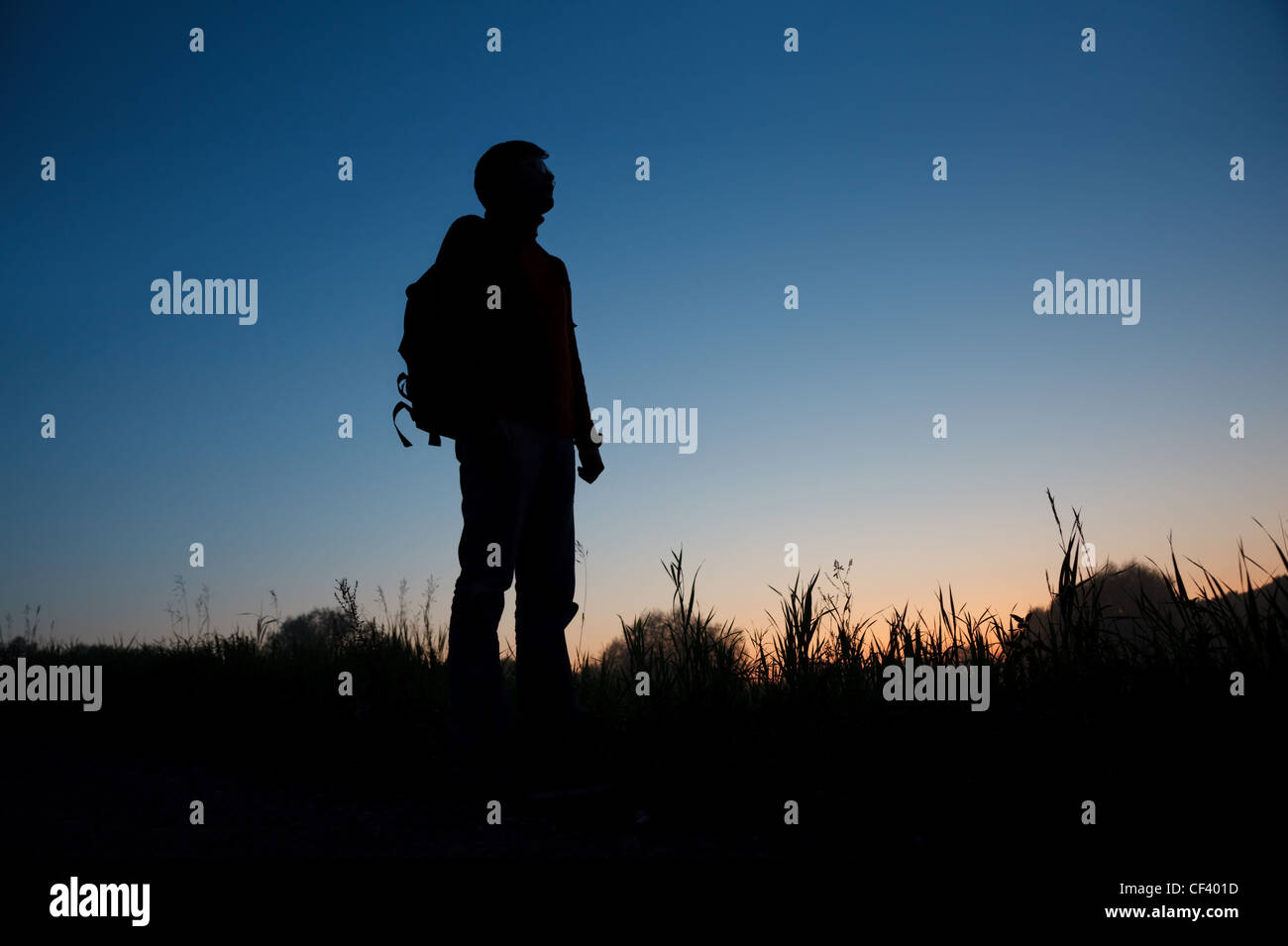 La silhouette di un uomo con uno zaino contro il cielo scuro Foto Stock