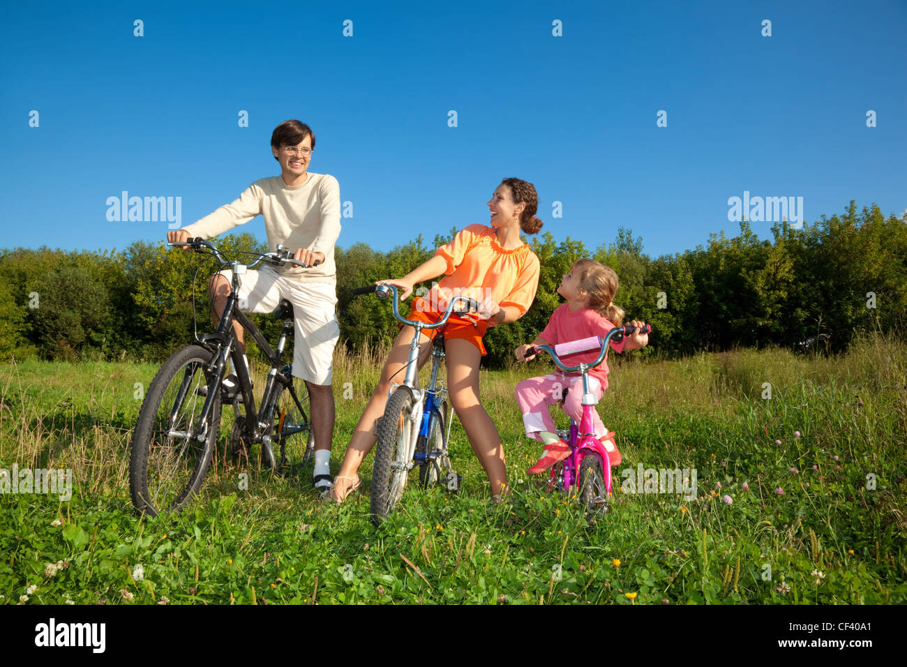 Famiglia da 3 persone su biciclette nel paese. La mamma con la figlia guarda il papà. Foto Stock
