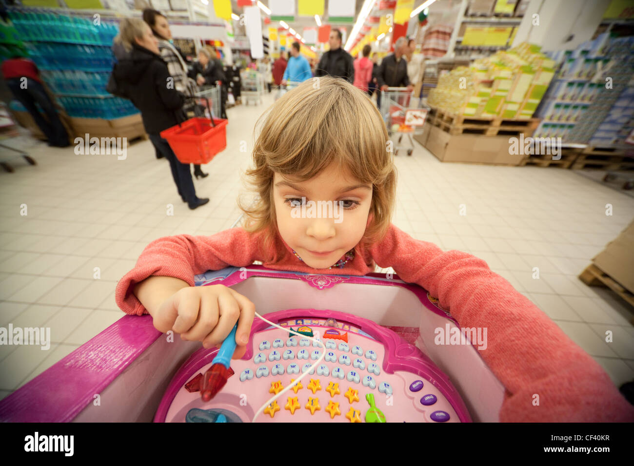 Piccola ragazza sedersi in shoppingcart ed esaminare il suo nuovo giocattolo Foto Stock