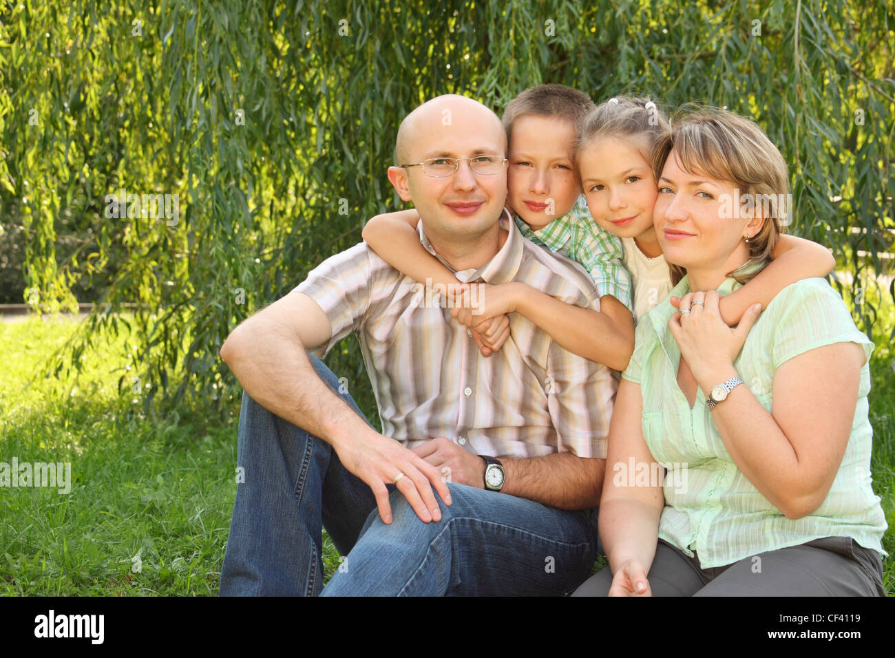 Famiglia con due bambini seduti presso l'erba nei pressi di vimini e guardando la fotocamera Foto Stock