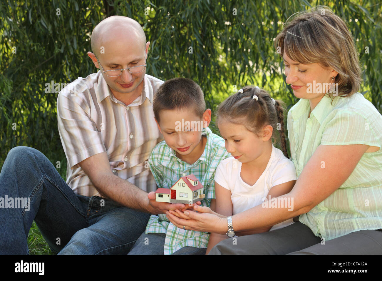 Famiglia in inizio di caduta park. padre, madre, poco un ragazzo e una ragazza è seduta sul prato nei pressi di vimini e guardando wendy house. Foto Stock