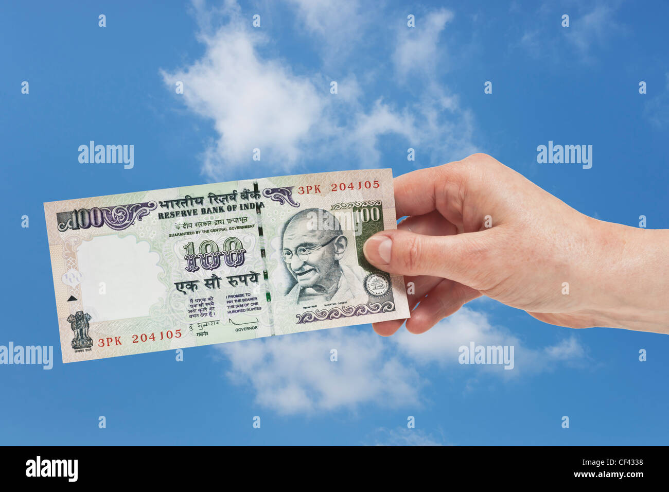 Un indiano 100 rupie bill con il ritratto del Mahatma Gandhi è tenuto in mano. Il cielo è in background. Foto Stock