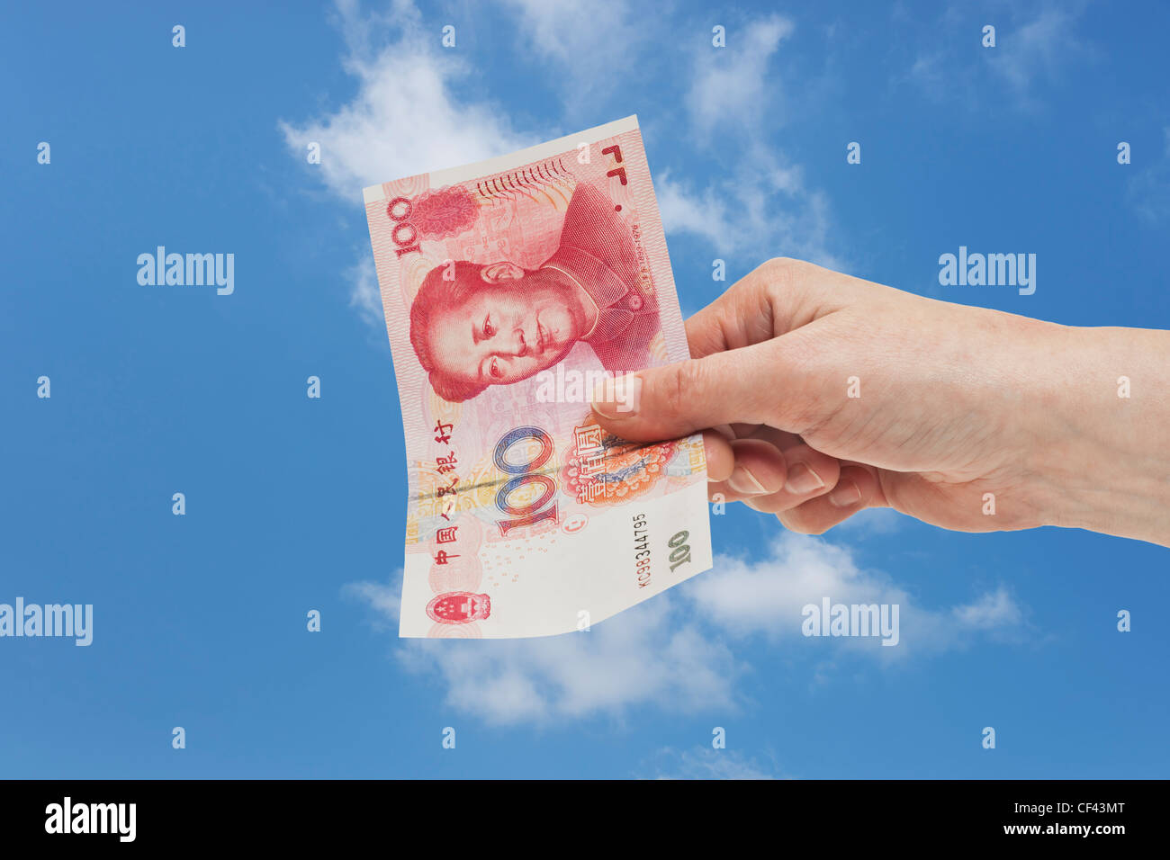 Uno cinese 100 Yuan bill con il ritratto di Mao Zedong è tenuto in mano. Il cielo è in background. Foto Stock