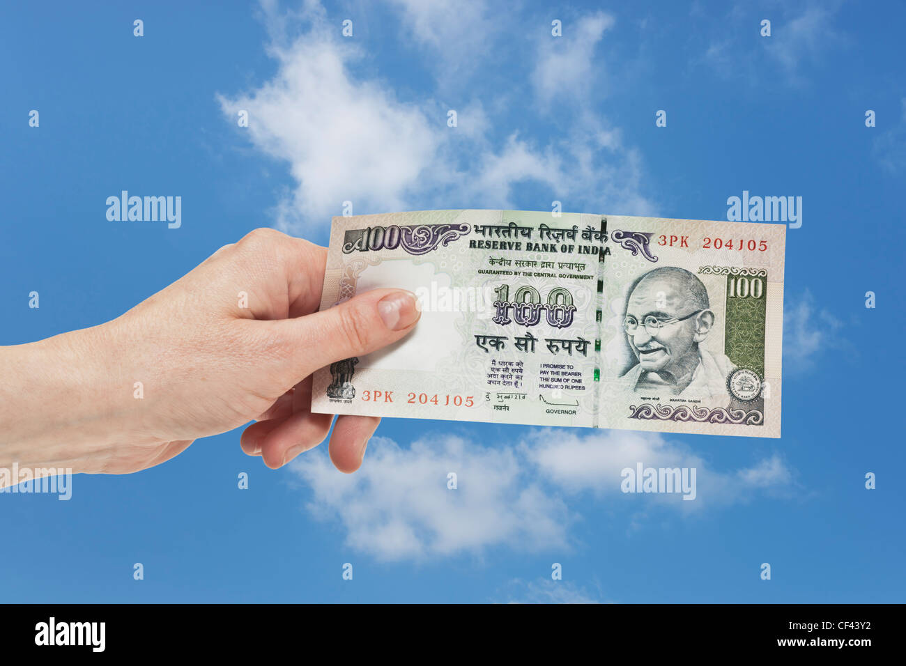 Un indiano 100 rupie bill con il ritratto del Mahatma Gandhi è tenuto in mano. Il cielo è in background. Foto Stock