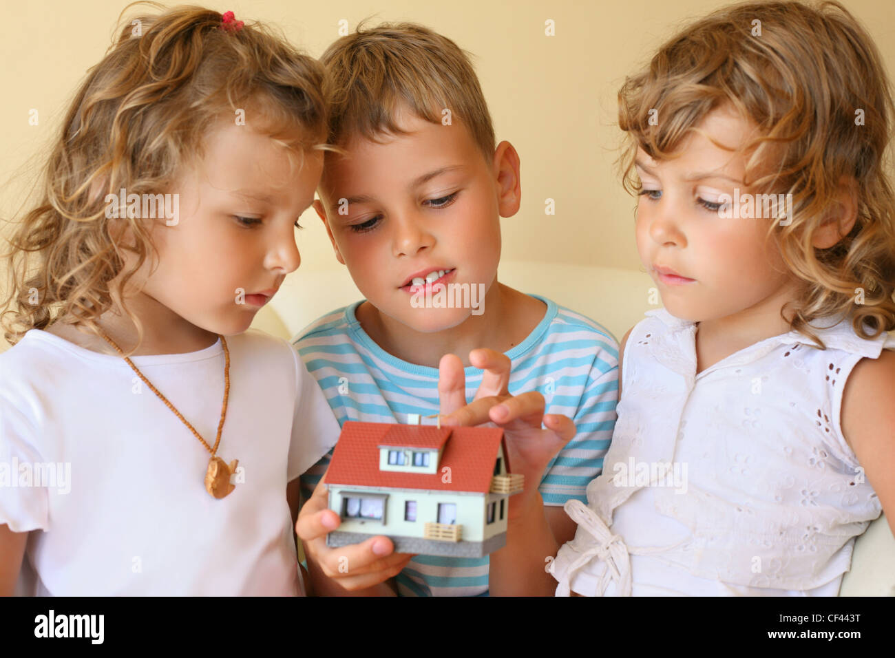 Bambini tre insieme tenendo le mani modello di casa in camera accogliente, boy tocca house dito Foto Stock