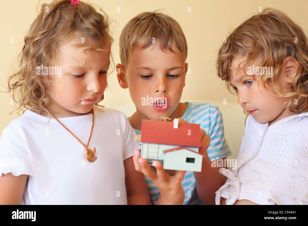 Bambini tre insieme tenendo le mani modello di casa in camera accogliente, due belle ragazze e ragazzo Foto Stock