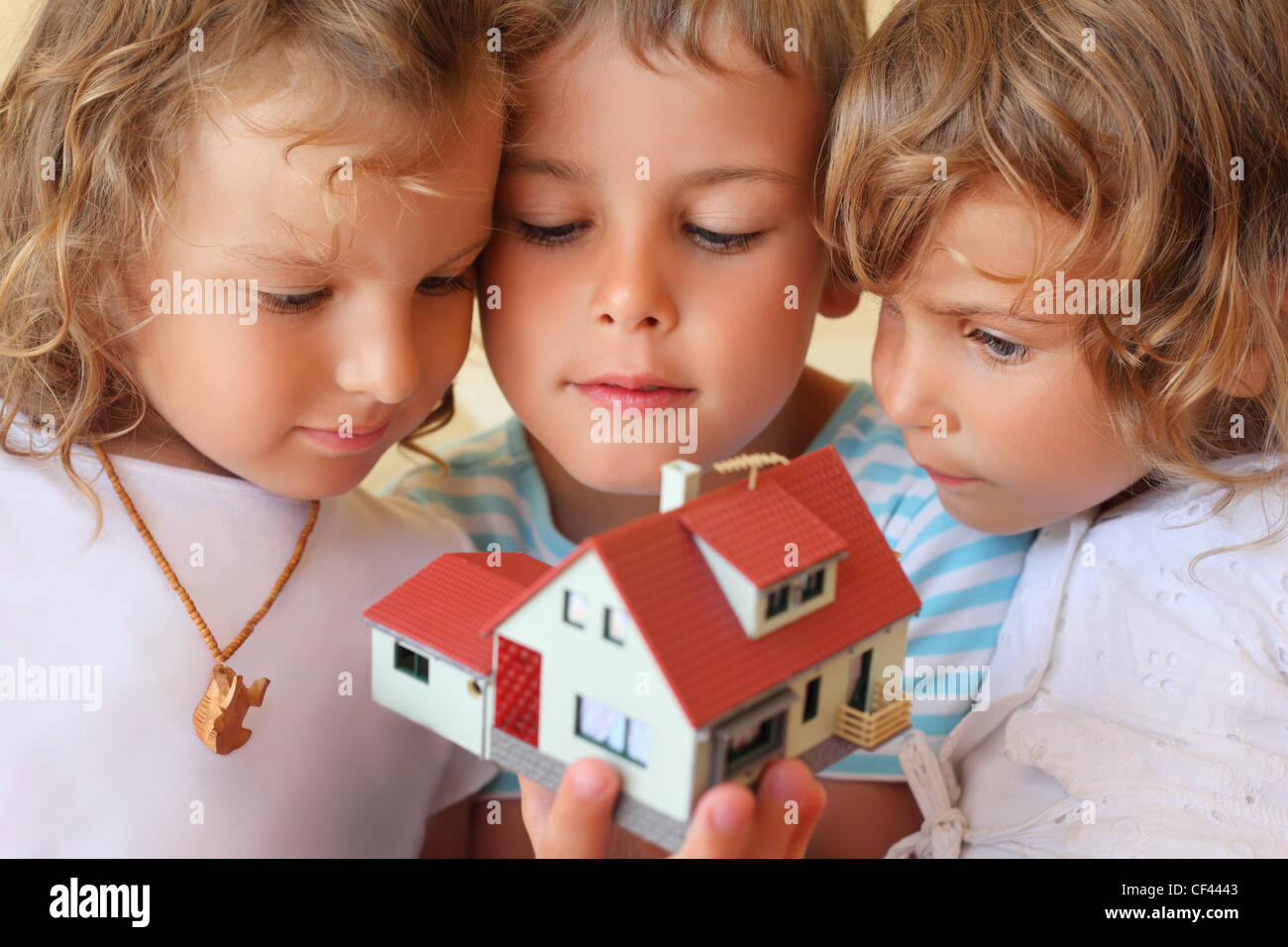 Bambini tre insieme tenendo le mani modello di casa in camera accogliente Foto Stock