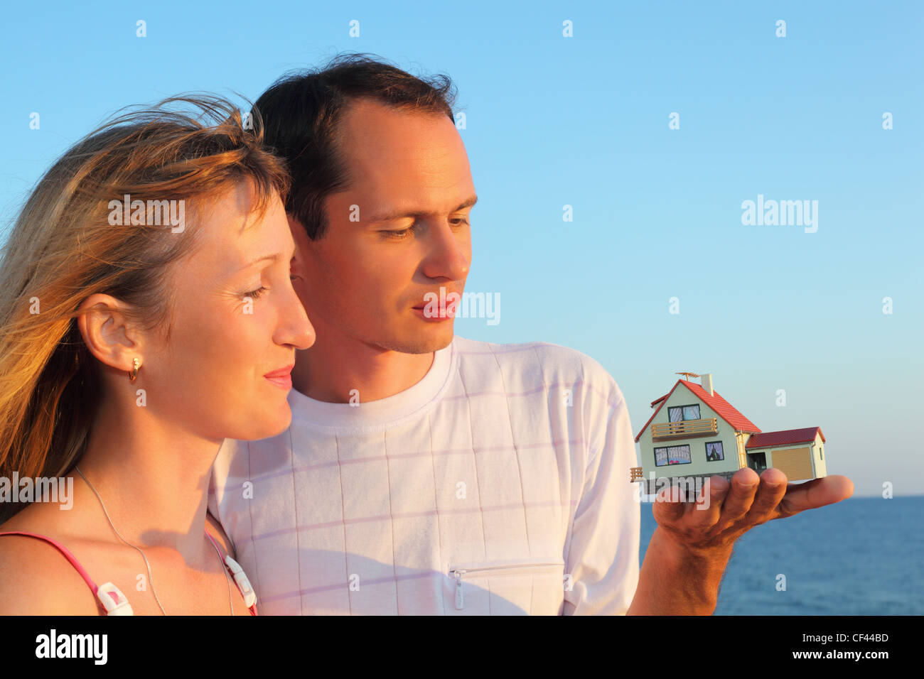 Giovane donna e uomo mantenendo in mani modello di casa con garage contro il mare in estate Foto Stock
