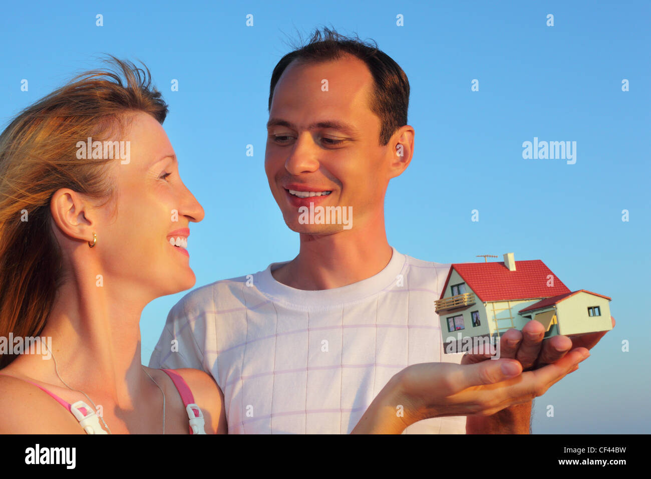 Giovane donna e uomo mantenendo in mani modello di casa con garage contro sky in estate Foto Stock