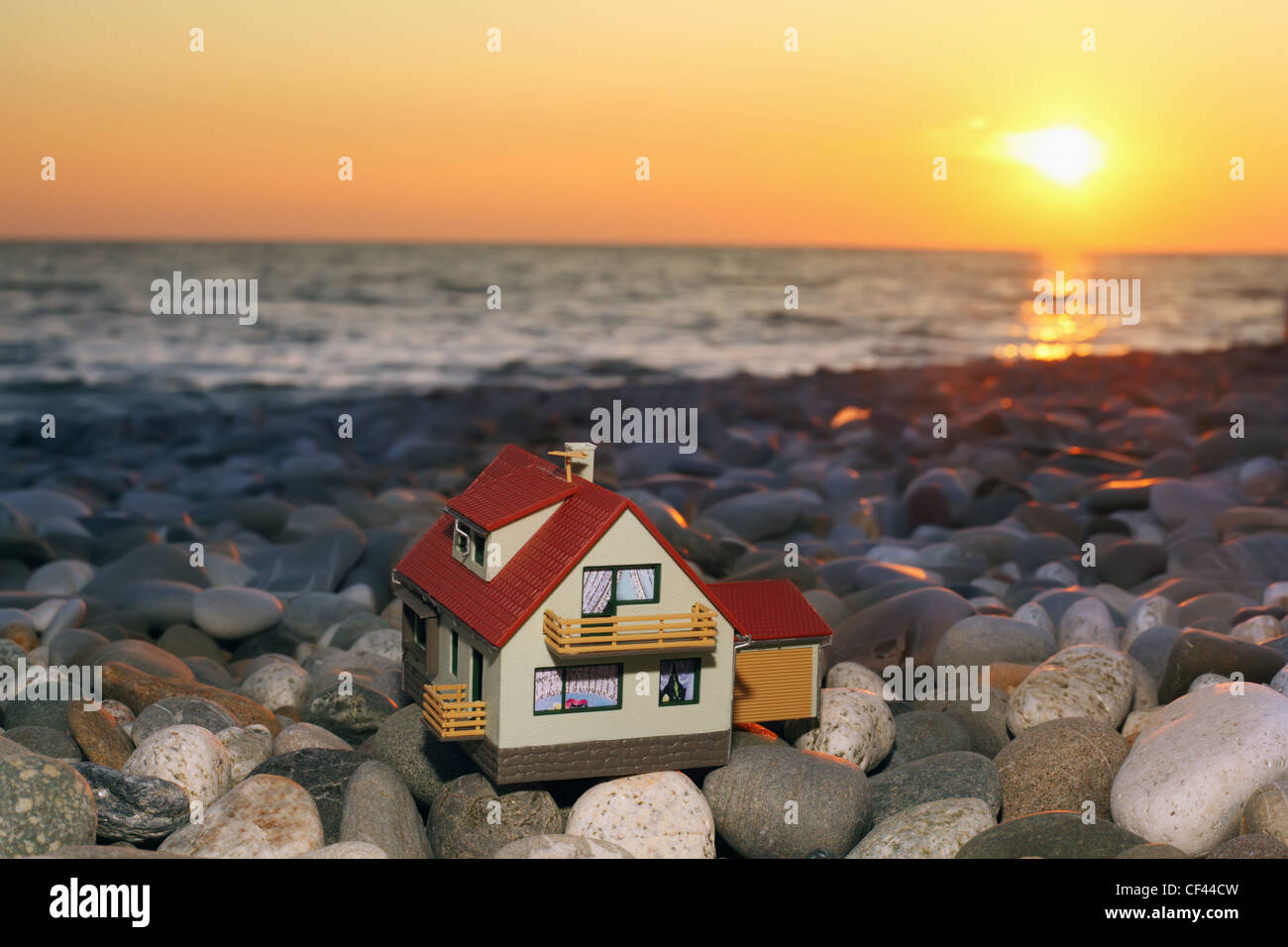 Modello di casa con garage sulla spiaggia sassosa in sera Foto Stock