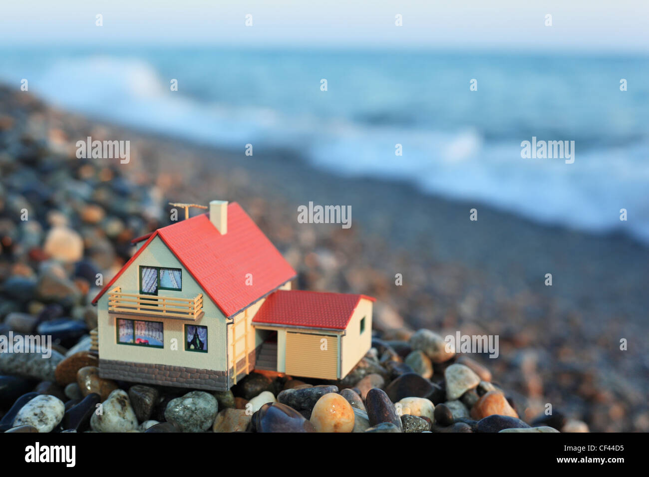 Modello di casa con garage sulla spiaggia sassosa in sera Foto Stock