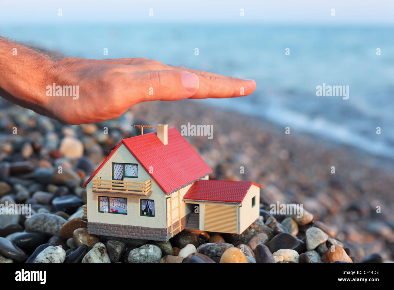 Modello di casa con garage sulla spiaggia sassosa in serata, mano d'uomo su house Foto Stock