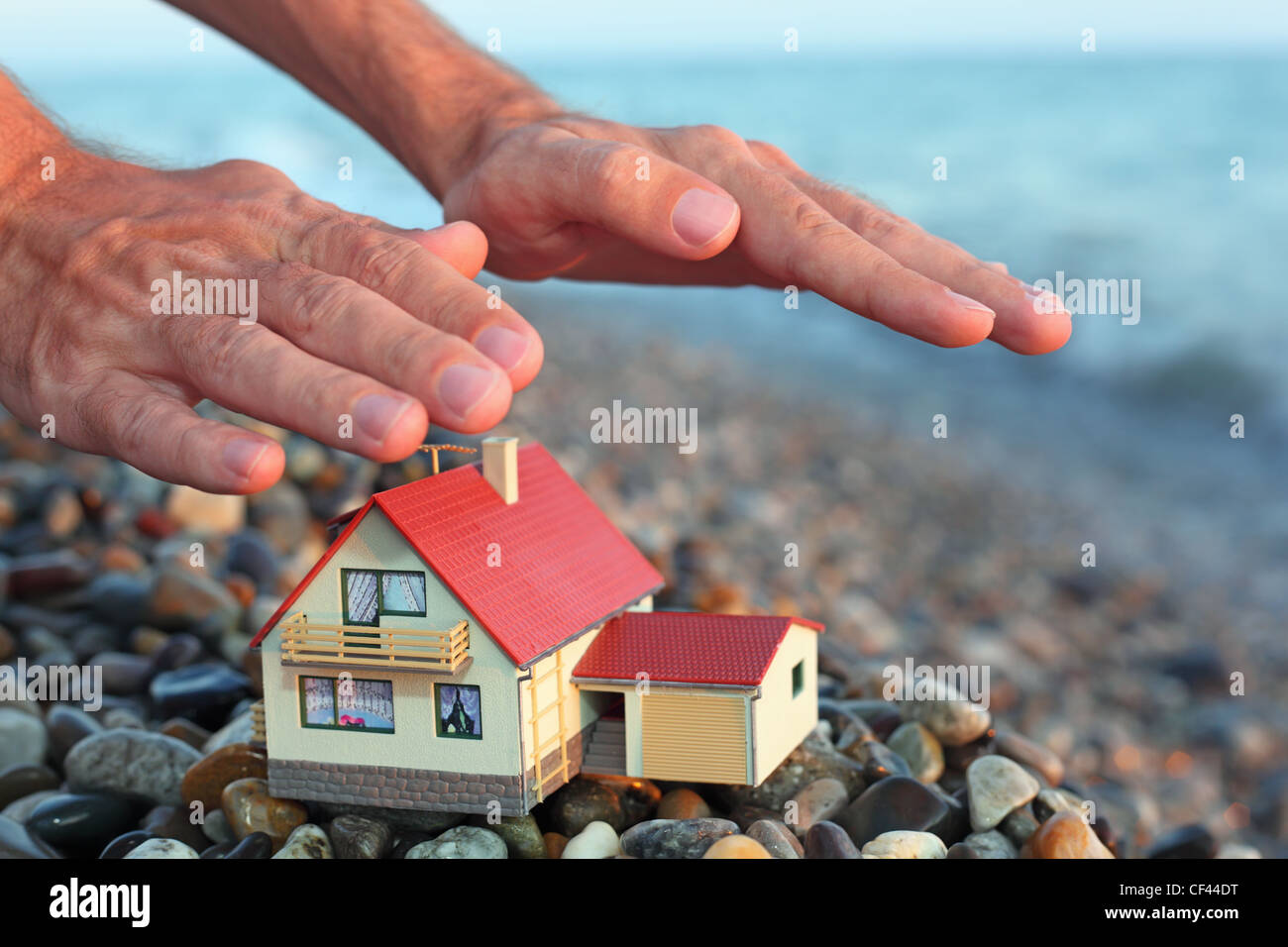 Modello di casa con garage sulla spiaggia sassosa in serata, mani dell'uomo su house Foto Stock