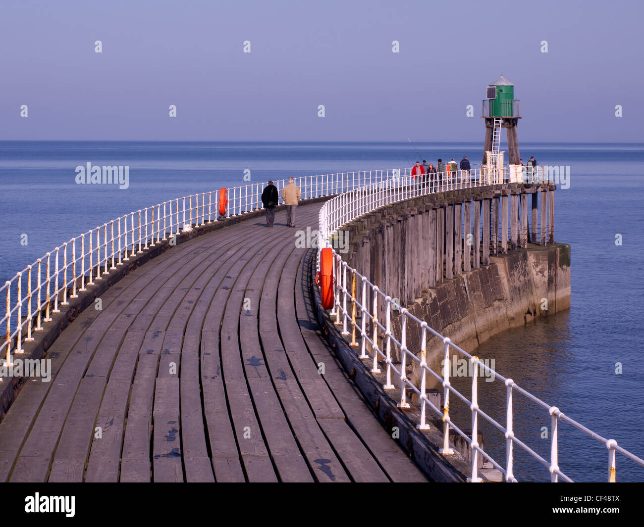 La gente che camminava sul Whitby Molo Ovest di estensione su una soleggiata giornata di primavera Foto Stock