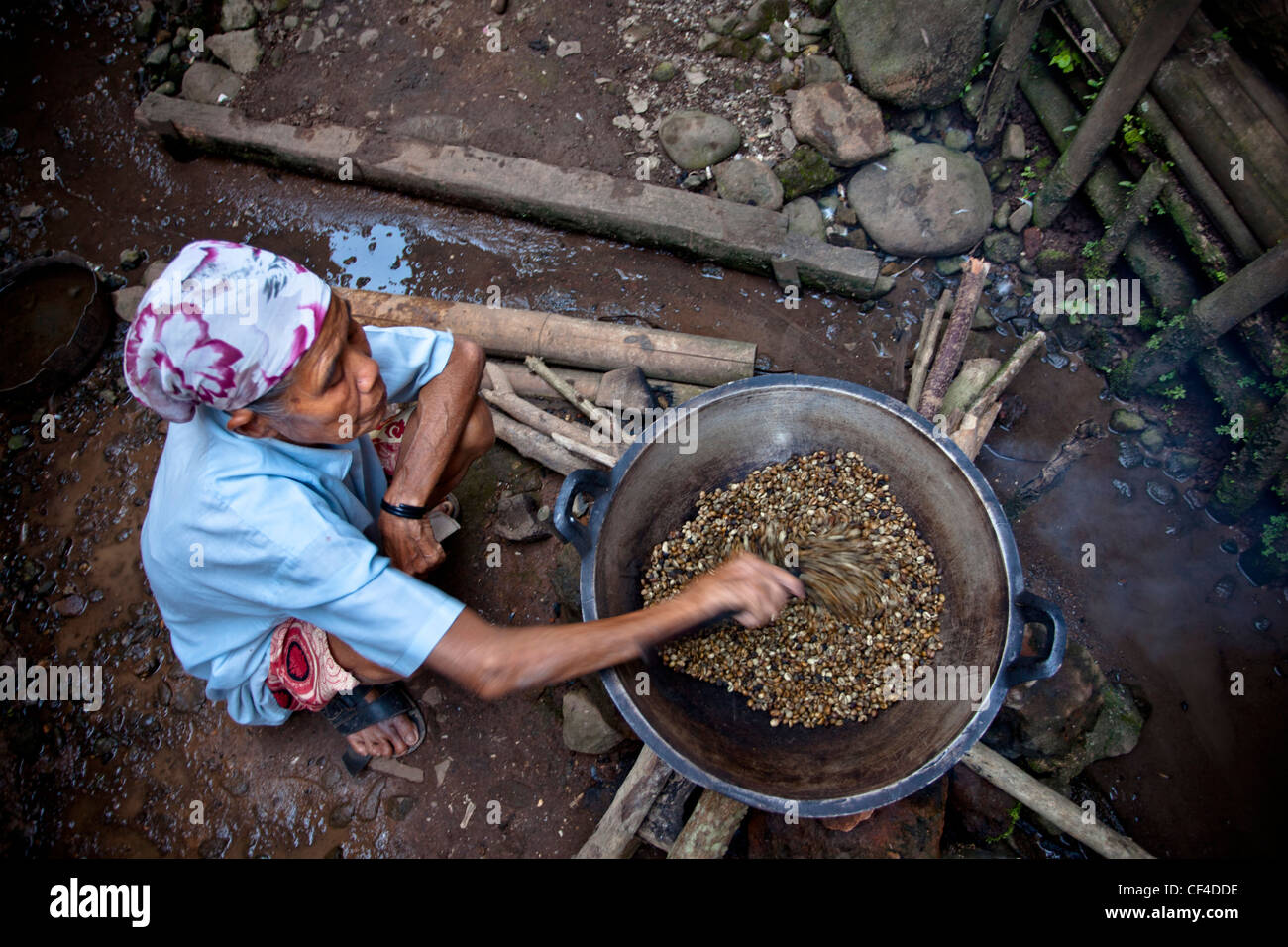 Senior donna agitazione i chicchi di caffè sul fuoco; Muara Pinang Indonesia Foto Stock