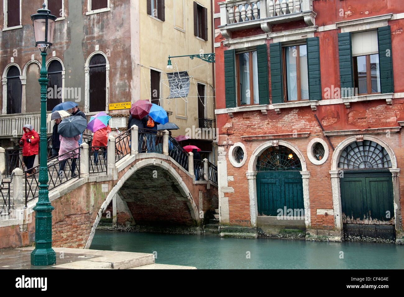 Gruppo di turisti con vivacemente colorato ombrelloni a piedi attraverso un ponte sul Canal, Venezia Italia Foto Stock