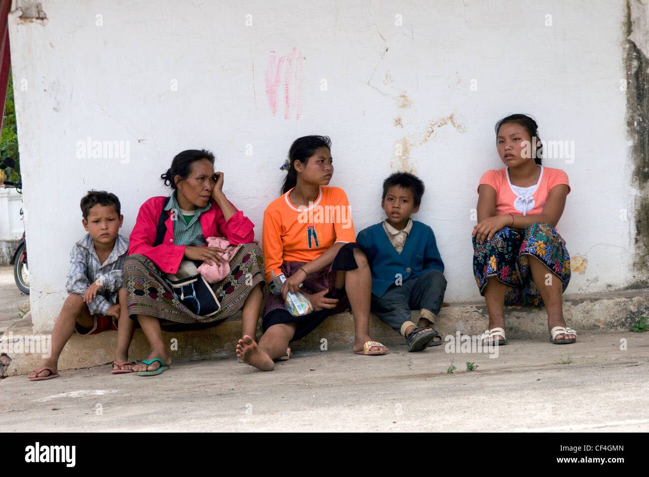 Una famiglia asiatica che vivono in condizioni di povertà è raccolto in un tempio in attesa per il Lao nuovo anno sfilano per iniziare a Luang Prabang, Laos. Foto Stock