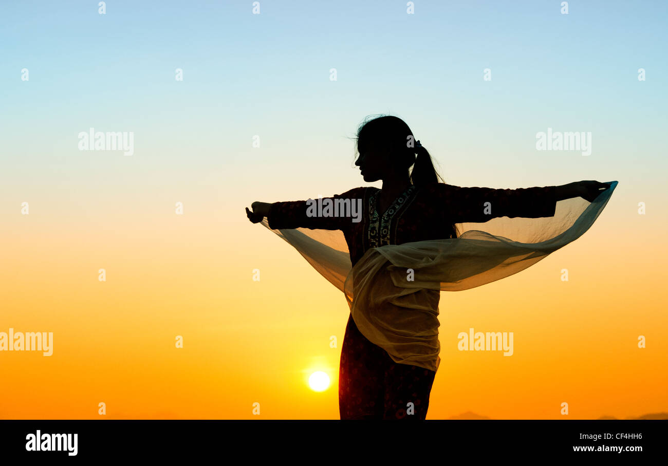 Ragazza indiana con velo passando nel vento verso il sole. Silhouette Foto Stock